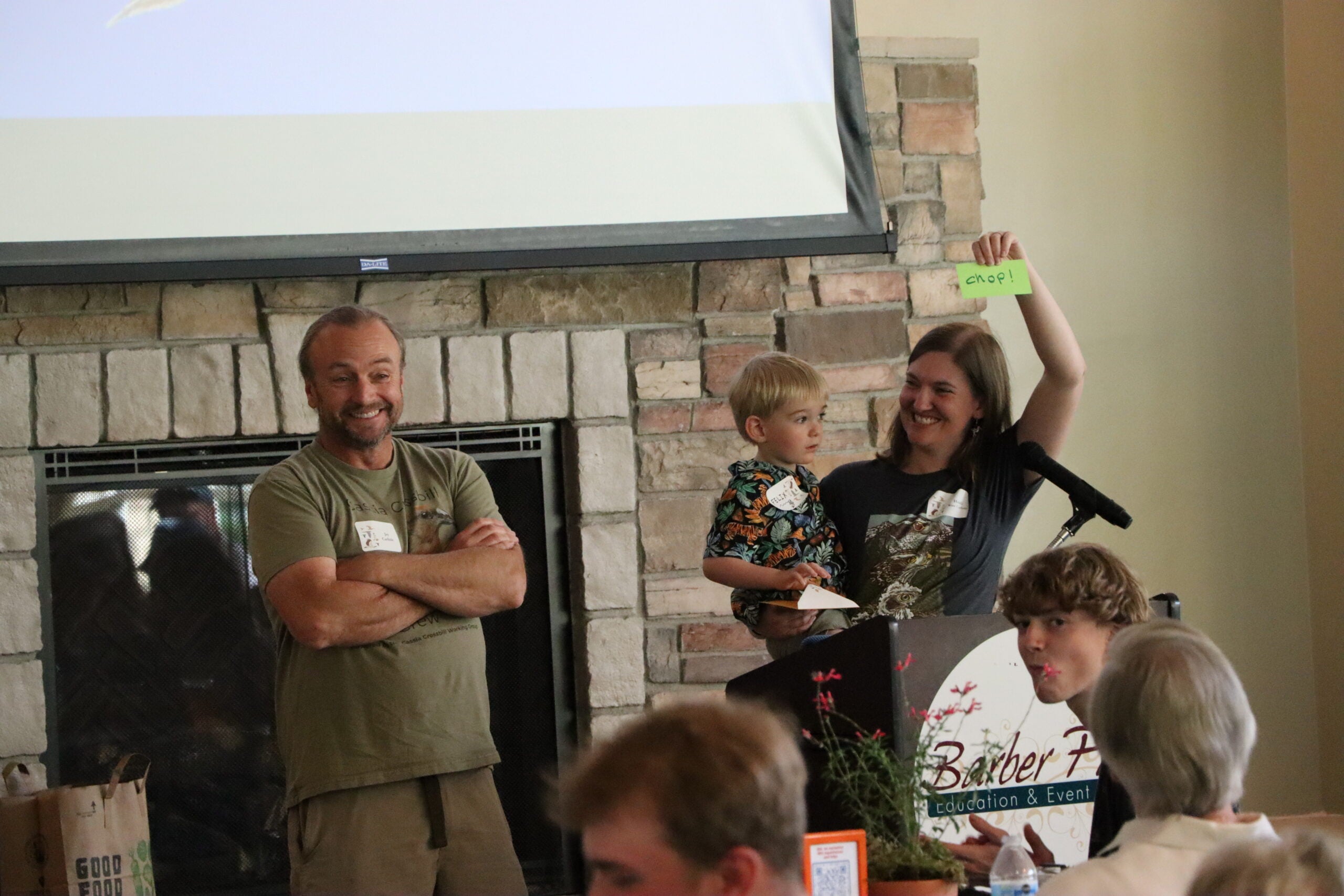 jay stands grinning on the left. on the right, Heidi holds their son, Felix, and a green card that says "chop!"
