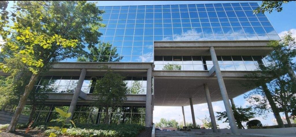 a shiny mirrored building perfectly reflects the sky, clouds, and trees around it
