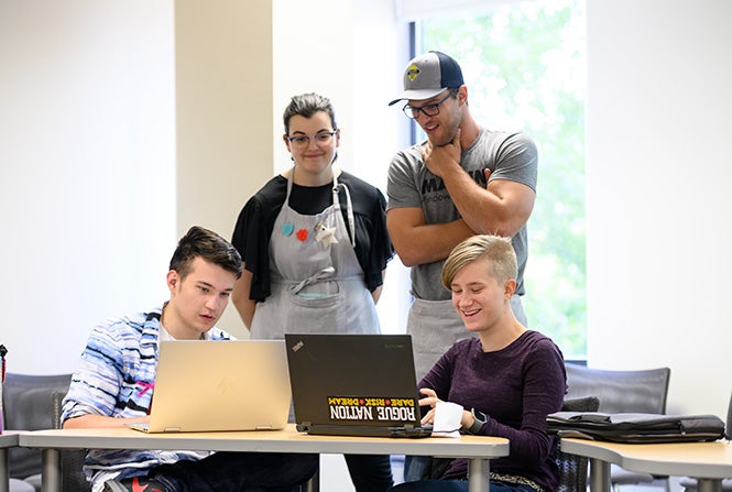 Two students using laptops with two MakerLab employees supervising them.