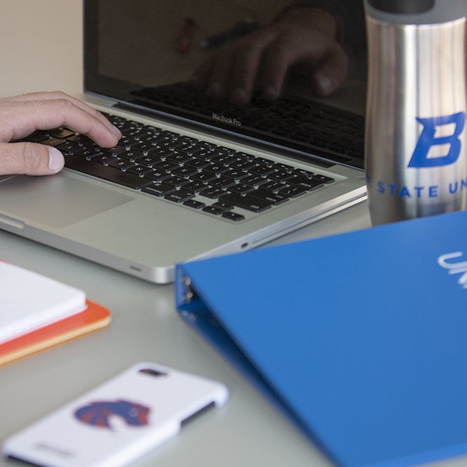 hand on keyboard of laptop with phone and notebook on desk