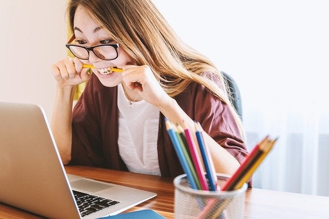 person biting a pencil, looking at a laptop screen