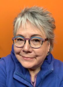 Elizabeth Ramsey wearing glasses and standing in front of an orange wall wearing a blue fleece
