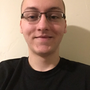 A young student with glasses standing in front of a wall.