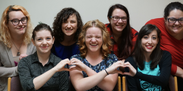 A posed photo of seven linguistics students in two rows. The three students in the front row are seated with their hands forming heart shapes