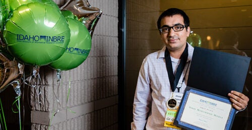 A man at a conference holds up his award.