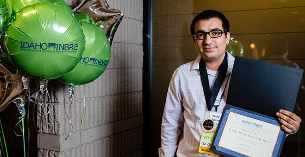 A man at a conference holds up his award.