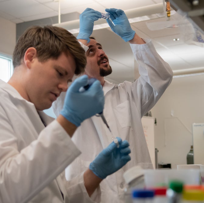 Professor in lab with student, holding up dish to look at it in the light