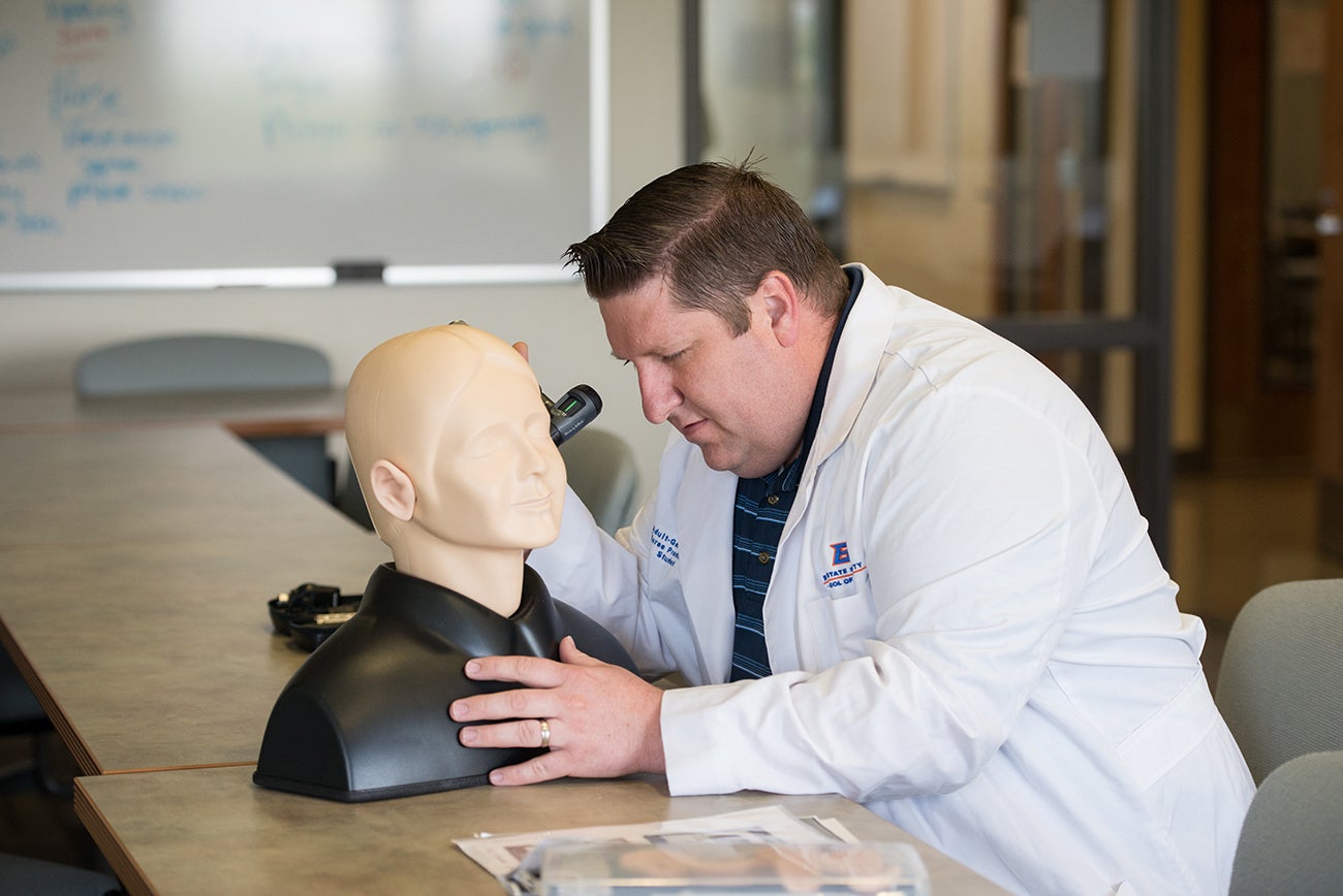 A man inspects the ear of a dummy patient.
