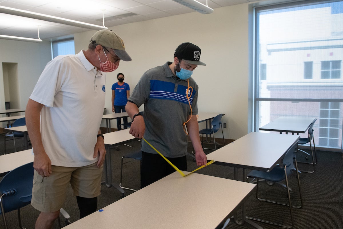 Joey Martinez and Lee Keily measure the distance between tables to set up for physically distanced classes.