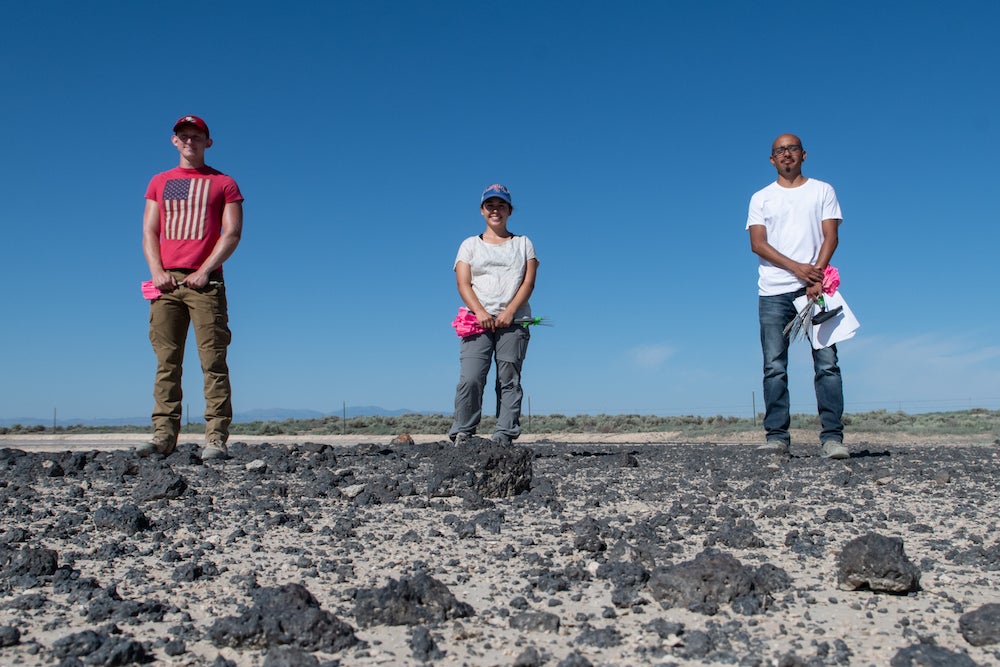 three people stand in desert holding marker flags