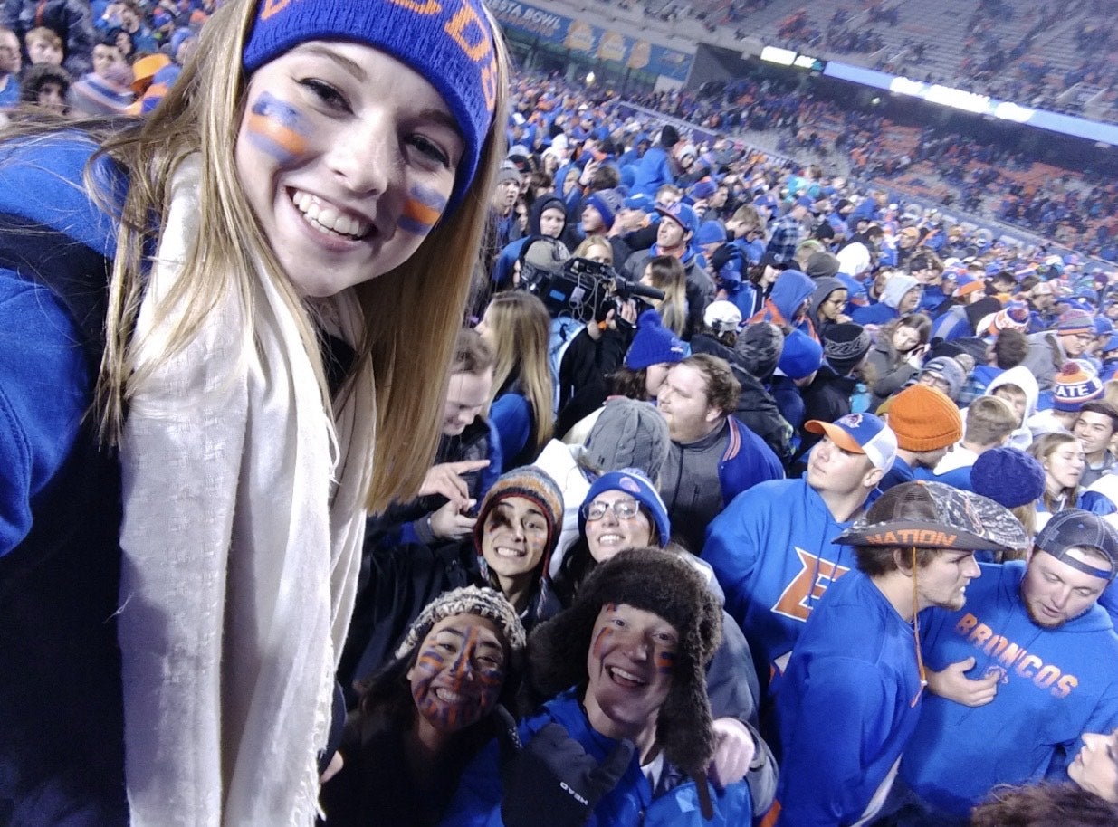 Students dressed in blue and orange school spirit fill a stadium. 