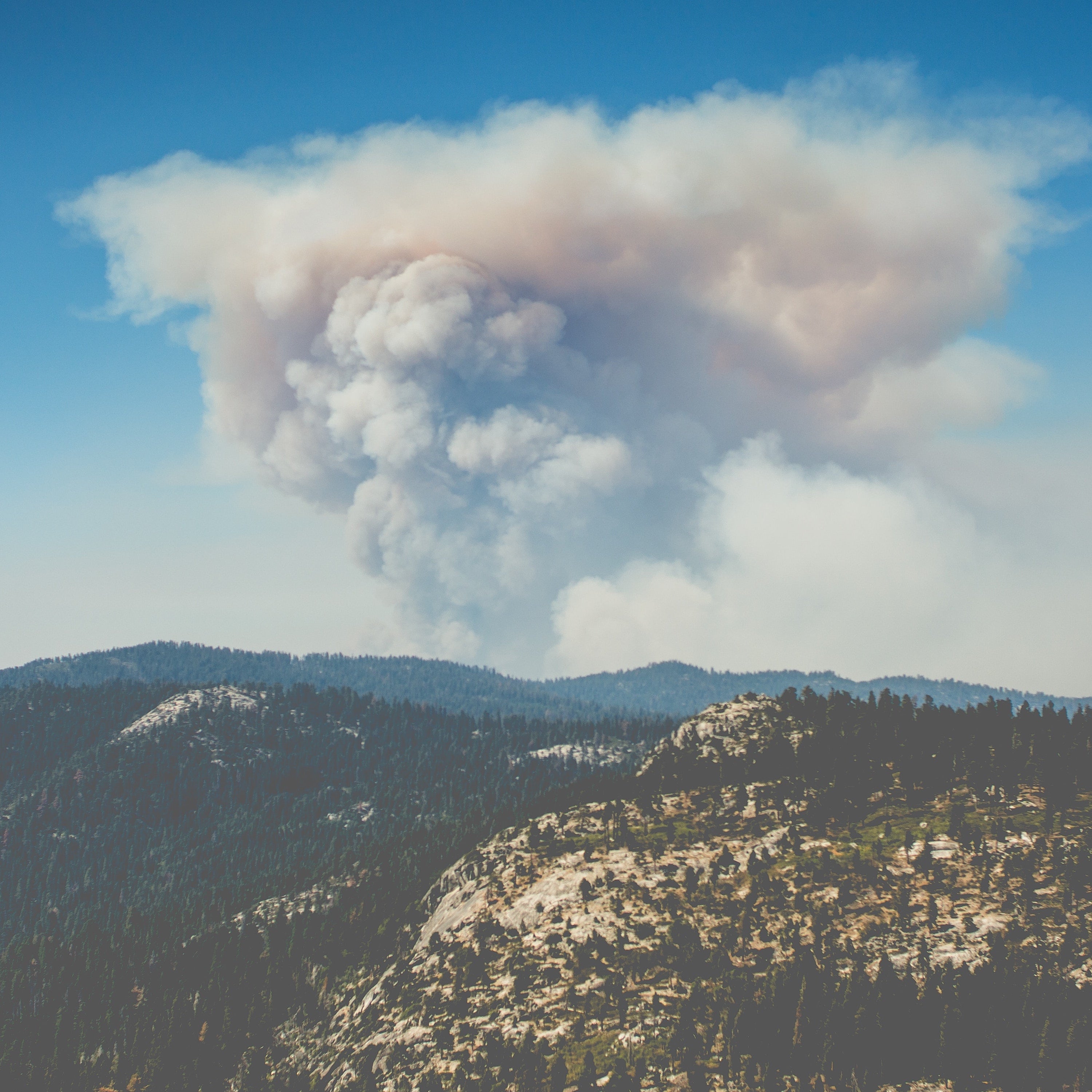 A large plume of smoke rises above mountains.