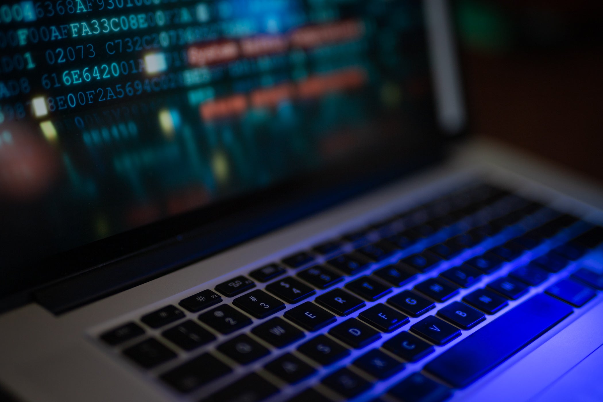 Close-up of a laptop keyboard with a screen displaying code and data in various colors.