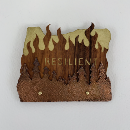 Wooden plaque engraved with the word "RESILIENT," featuring trees and flames symbolizing strength.
