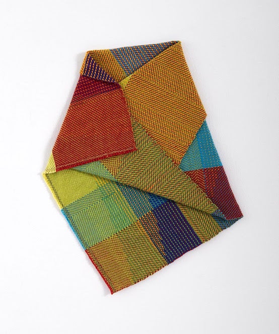 Vibrant geometric-patterned fabric folded neatly, showcasing intricate herringbone and diagonal designs in shades of red, orange, yellow, green, blue, and purple. 