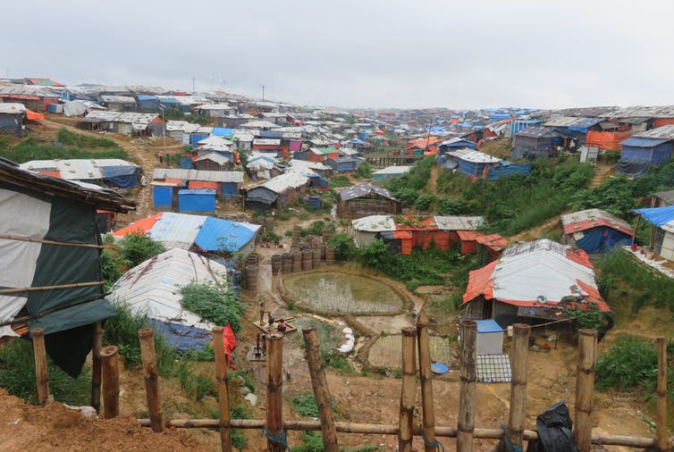 Tents in a Rohingya refugee camp cluster on a muddy hillside.