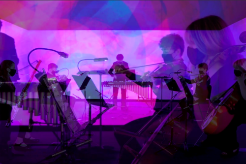 Musicians performing under vibrant purple and pink stage lights with violins, marimba, and other instruments in view.