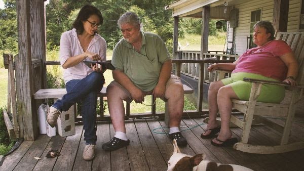 The people and a dog sit together on a wooden porch. 