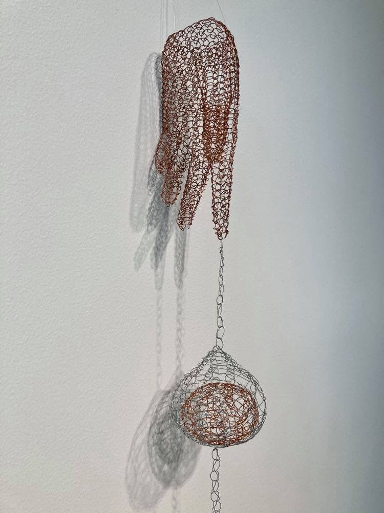 Copper and steel wires shape a hand with a ball draping down from a finger. 