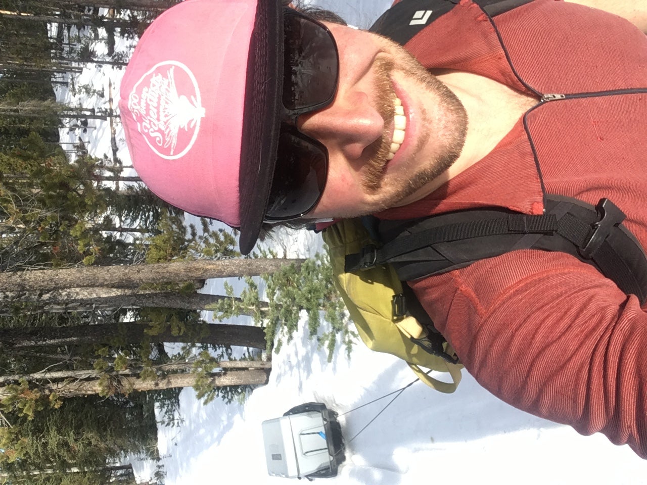 student in coat and ball cap hauls sled of car batteries through now in densely wooded mountain