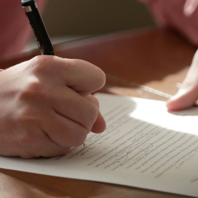 A man writes on a piece of paper with a pencil