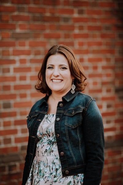 Sara smiles and stands in front of a brick wall