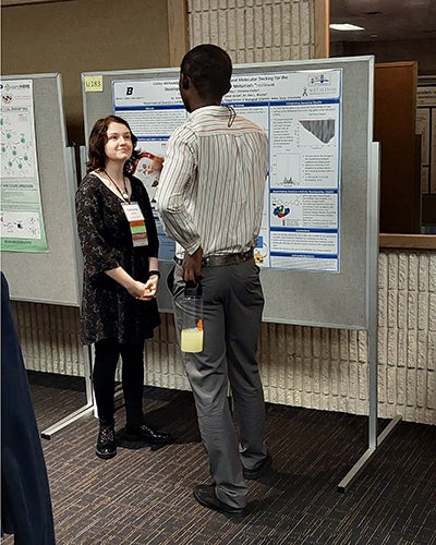 young woman explains research poster to bystander
