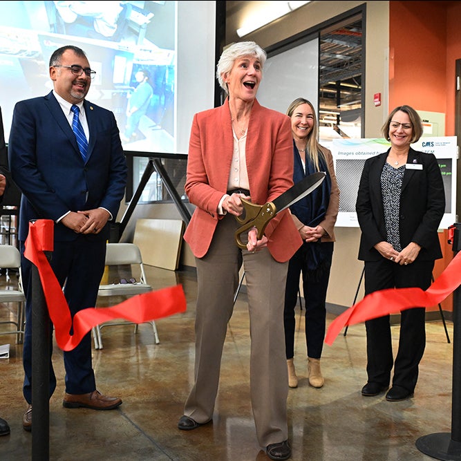 one woman cuts red ribbon with large scissors, surrounded by three Boise State colleagues