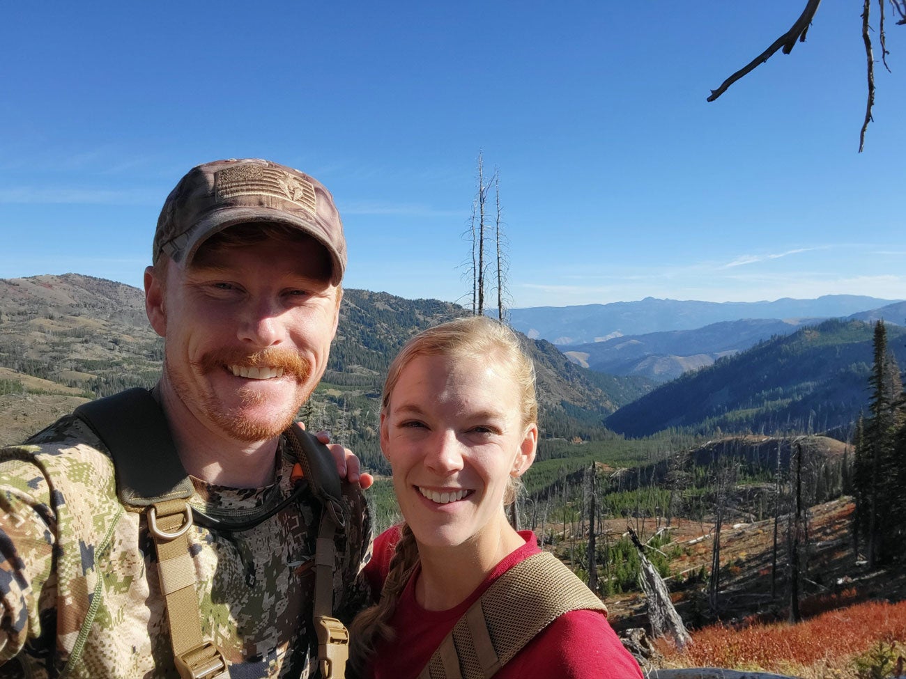 Joseph and Hannah Potter smile on a hilltop with mountain sprawling in the background under a blue sky.