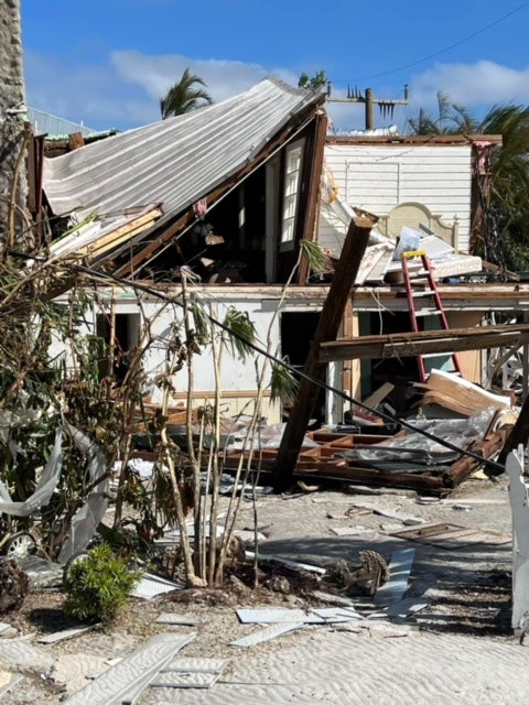 A dilapidated house surrounded by post-hurricane debris.