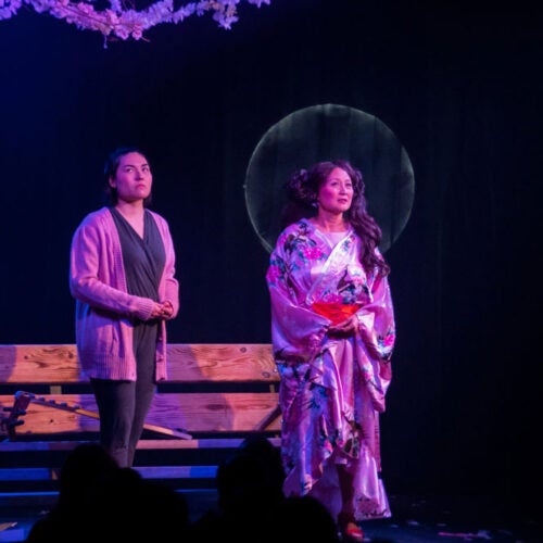 Janet Lo stands in blue lighting on a stage with two other women.