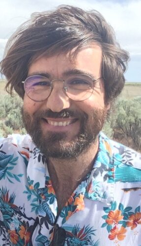 man in Hawiian flower shirt smiles in front of sagebrush