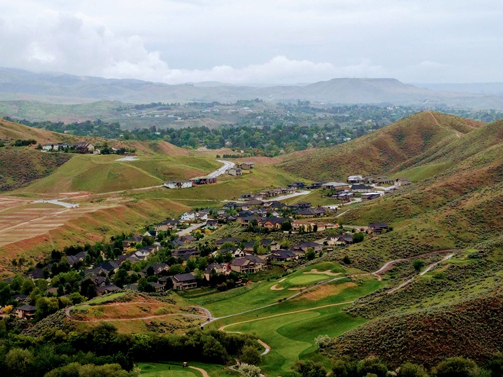 a subdivision extends up the side of a green foothill