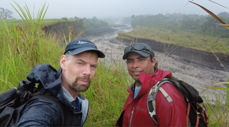 Two men stand beside large drainage pass filled with lahar