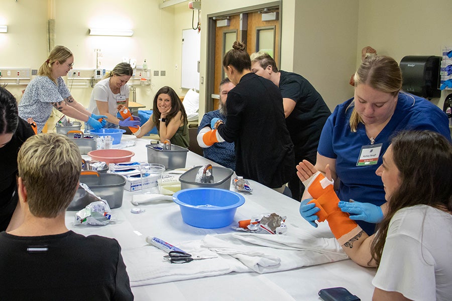 Nurse practitioner students practice putting casts on people's arms who sit around a table.