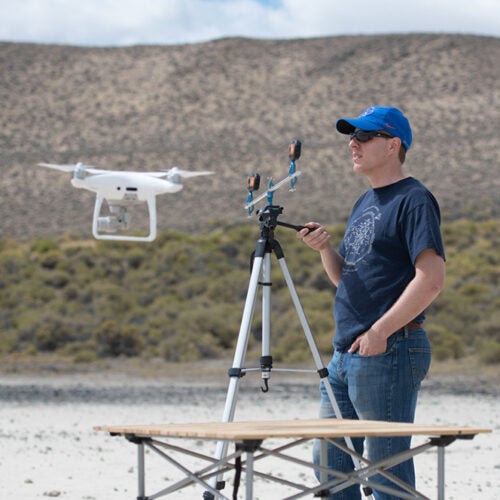 man stands at control station, while drone hovers in front of him