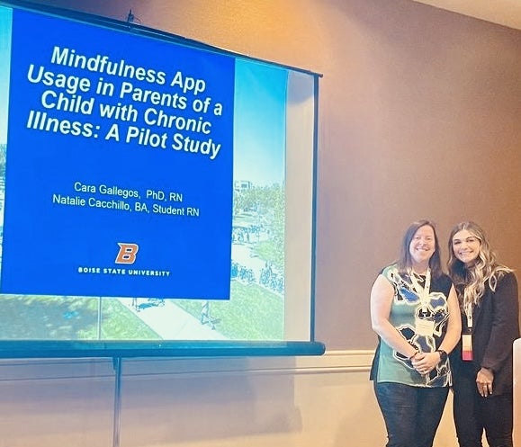 Dr. Cara Gallegos and research assistant Natalie Cacchillo pose next to a projector screen with their research presentation on it.