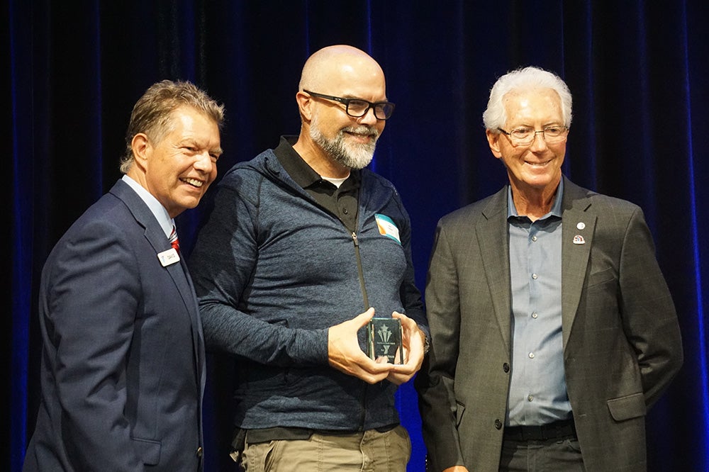Max Veltman stands in between two YMCA representatives and holds a small glass plaque.