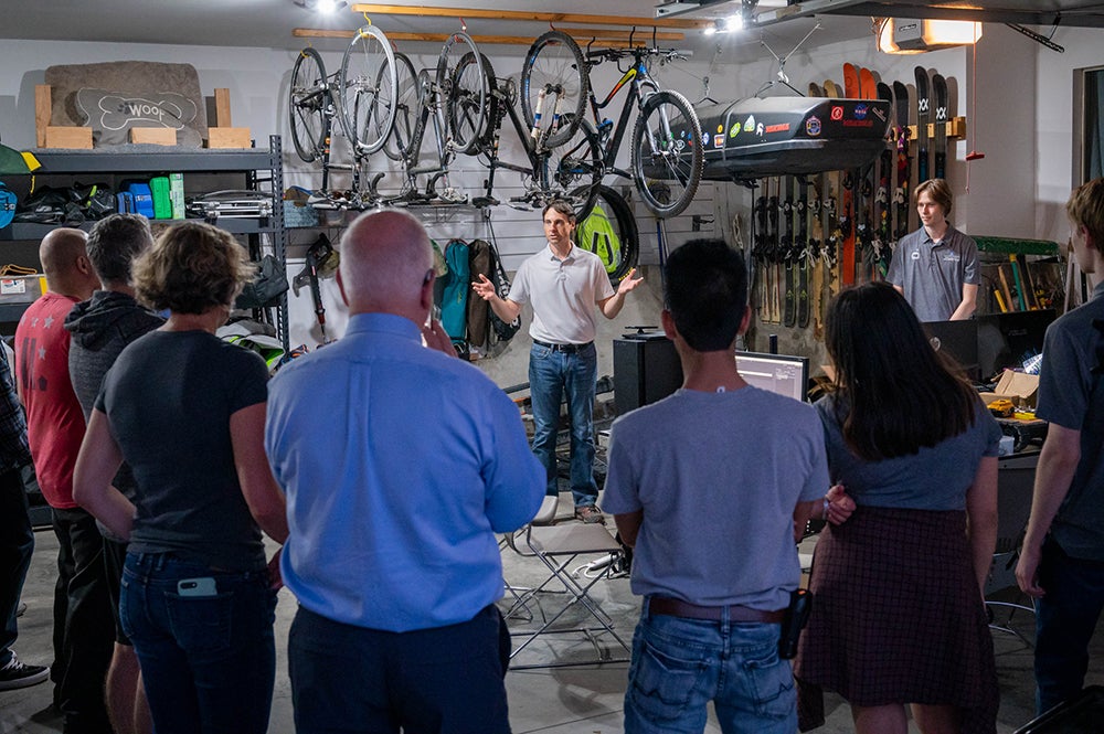 man stands in a garage surrounded by semicircle of students