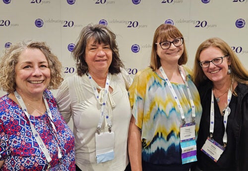 Paula Molina-Shaver, Tammie Sherner, Tracee Chapman and Kelley Connor stand together in from of a conference banner.