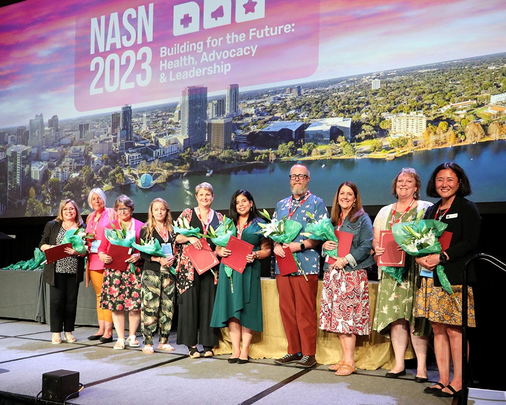 Douty stands on stage with 9 other people to accept an award at a conference.
