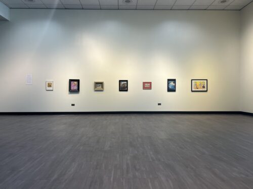 Art exhibit featuring seven framed pieces along a white wall.