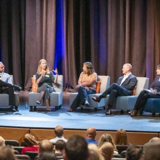 A group of people sit on a stage for a discussion in front of an audience