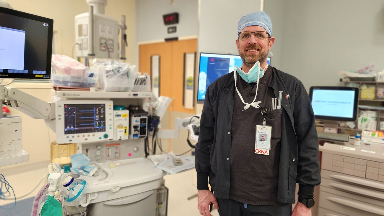 Justin Malinosky stands in his scrubs, smiling in the operating room.