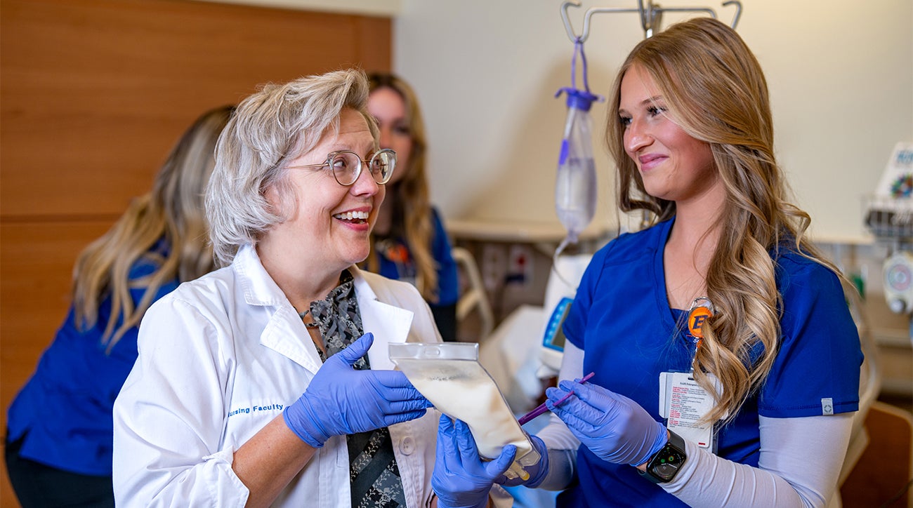 Amy and a nursing student look at a bag used for feeding patients.