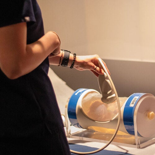 Sonography student in scrubs holds ultrasound probe against a fetus phantom