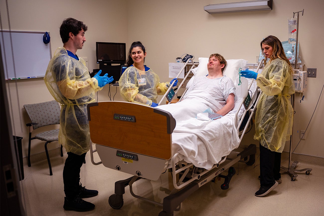 Three nurses attend to a patient in a hospital room.