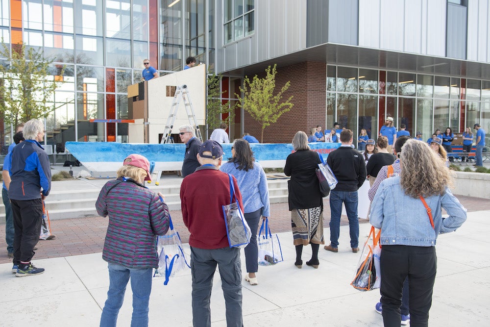 people walk past Micron engineering building where students are constructing some sort of structure