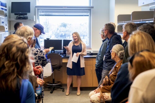 woman in center of lab speaks to group of about 20 people