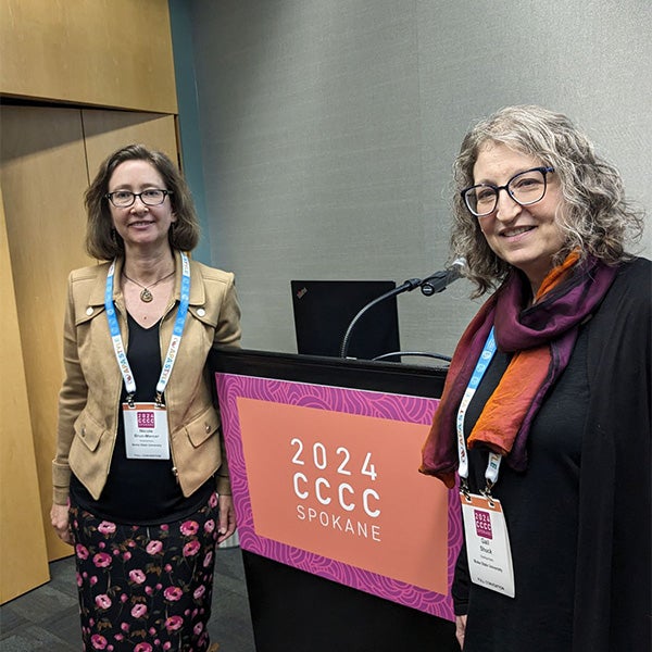Suck and Brun-Mercer posing in front of a podium at a conference.